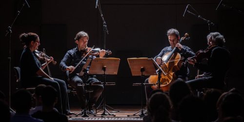 Os quatro membros do Quarteto de Cordas da Cidade de São Paulo sentados em círculo tocando seus respectivos instrumentos.